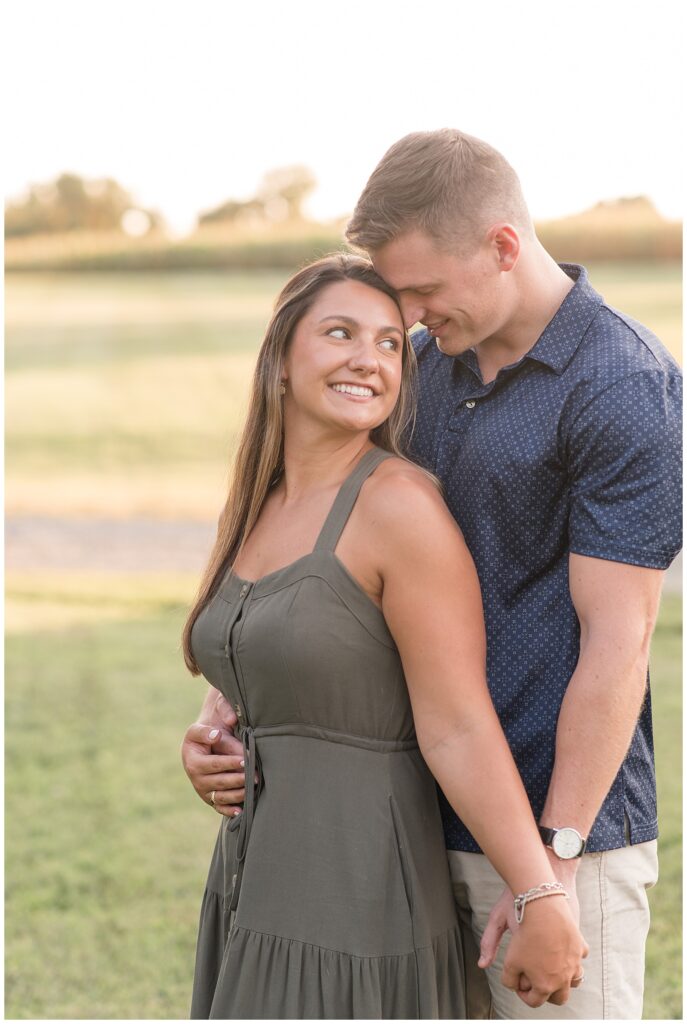 guy hugging girl from behind as they hold hands at sunset in chesapeake city maryland