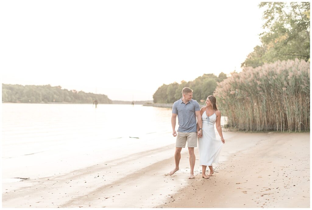 couple holding hands and walking along beach in maryland at sunset in chesapeake city