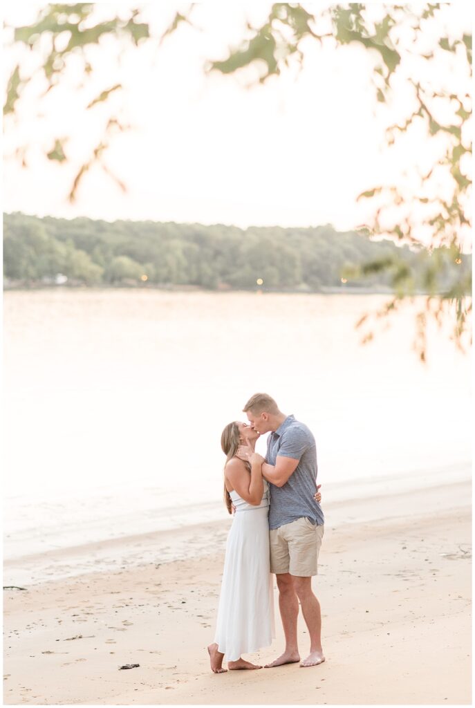 couple kissing on beach with water behind them at sunset in chesapeake city maryland