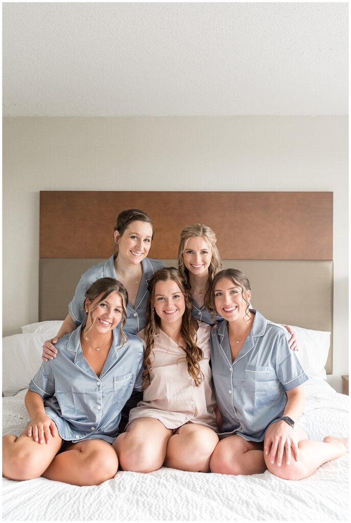 bride and her four bridesmaids sitting on bed in robes all huddled together in hotel room in flourtown pa