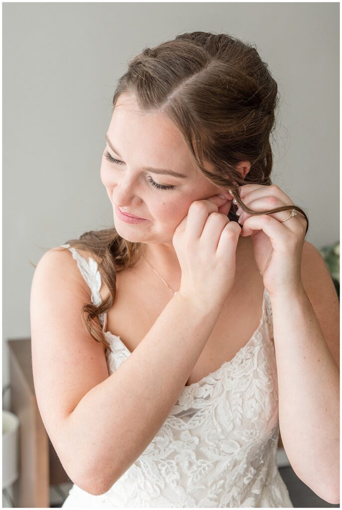 bride putting her left earring into her ear with white lace spaghetti strap wedding gown in pennsylvania