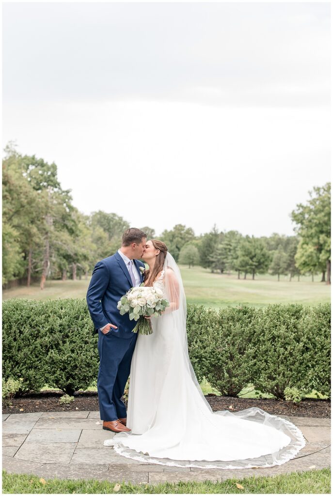 couple kissing with golf course behind them at flourtown country club