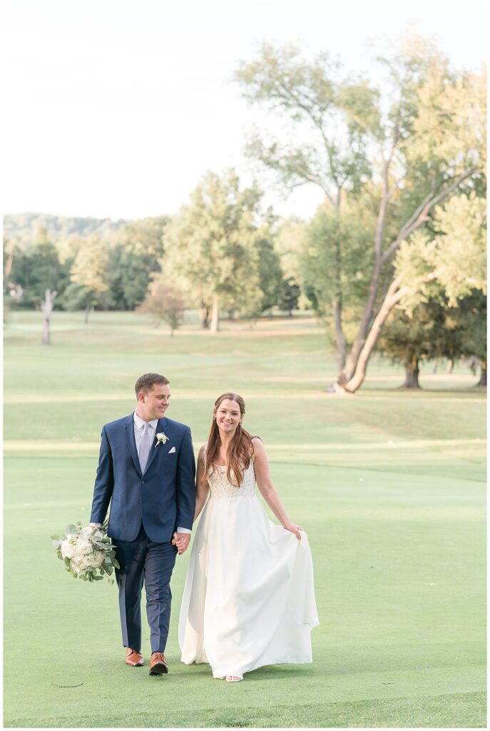 couple holding hands and walking towards camera on grass fairway at flourtown country club