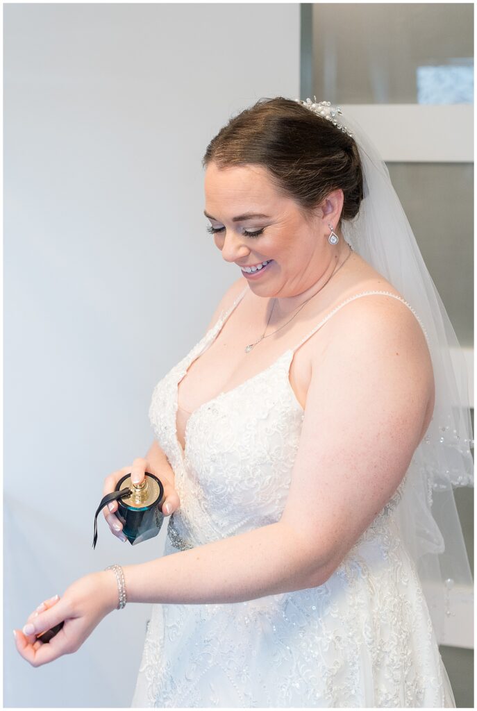 bride in spaghetti strap white gown spritzing her left wrist with perfume at jumping brook country club