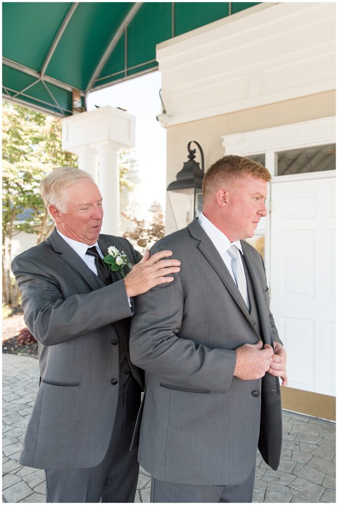 groom's father helping him to get his gray suit coat on in new jersey