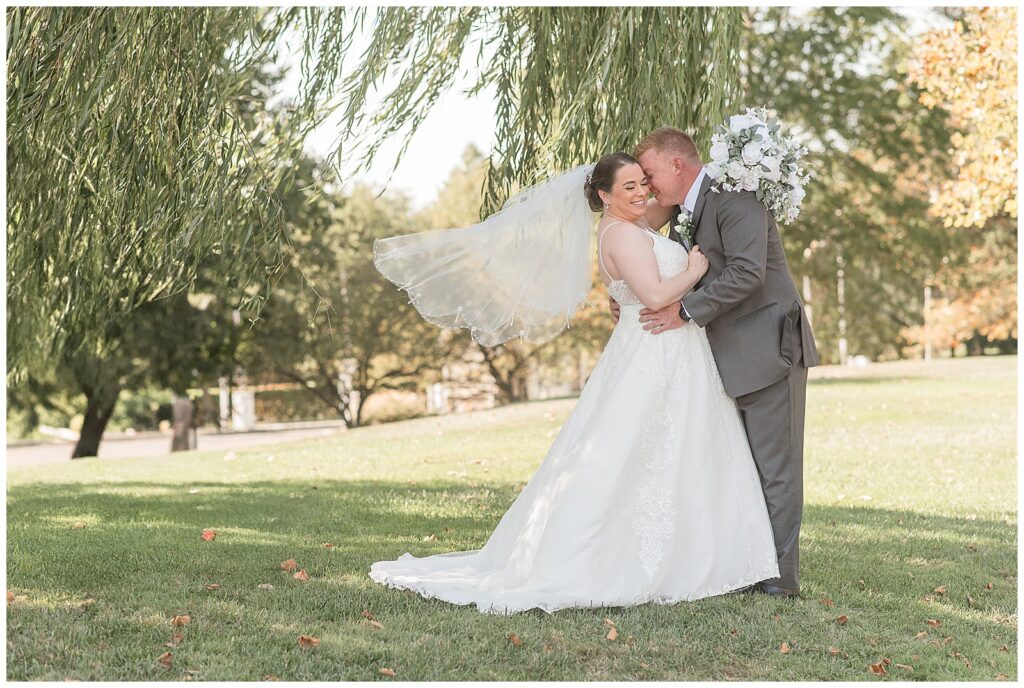 groom kissing his bride as she dips back slightly by willow tree at jumping brook country club in new jersey