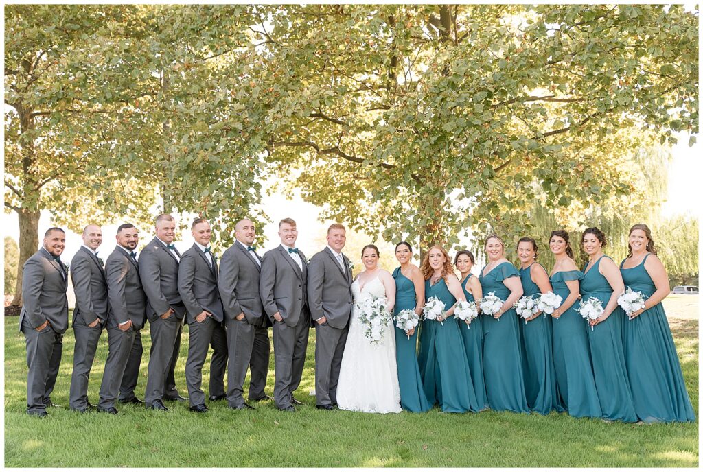 couple with their bridal party by trees at jumping brook country club in new jersey