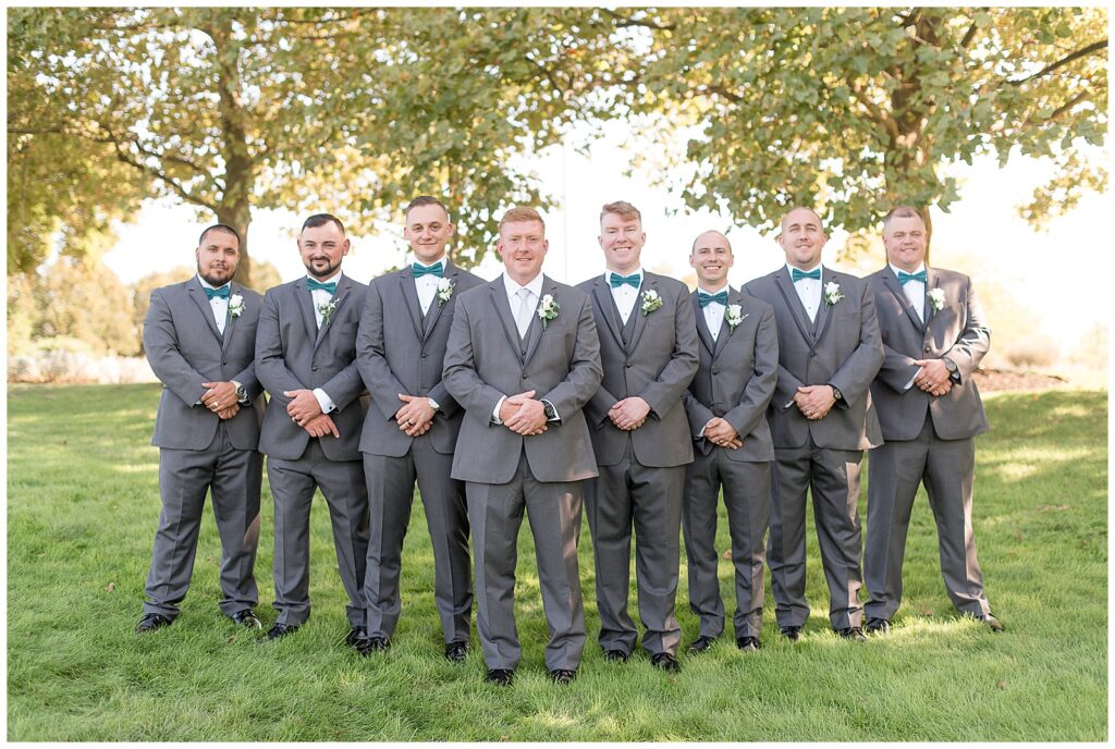 groom with his seven groomsmen all wearing dark gray suits and standing in a v formation in new jersey