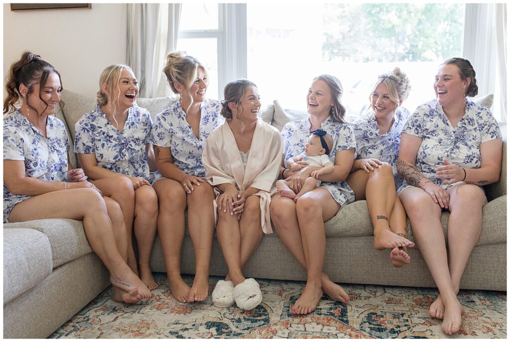 bride surrounded by her six bridesmaids all in robes on couch before wedding at bride's family farm