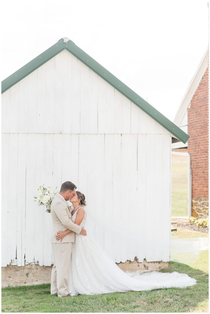 couple kissing by small white and green barn on sunny fall day in pennsylvania