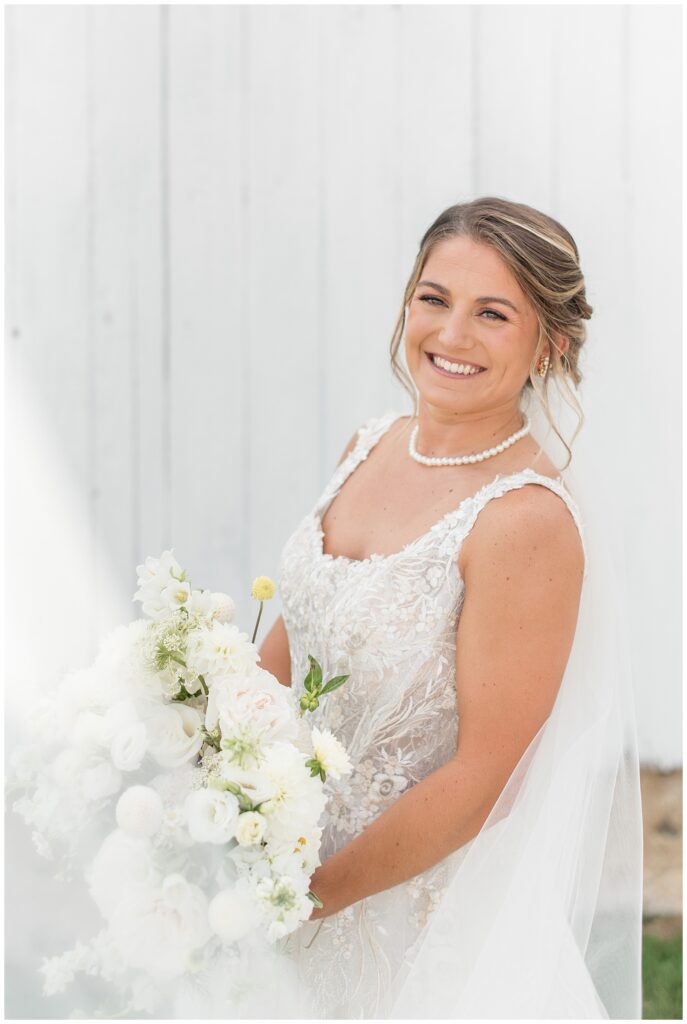 bride holding her bouquet of white flowers in sleeveless gown by white barn in pennsylvania