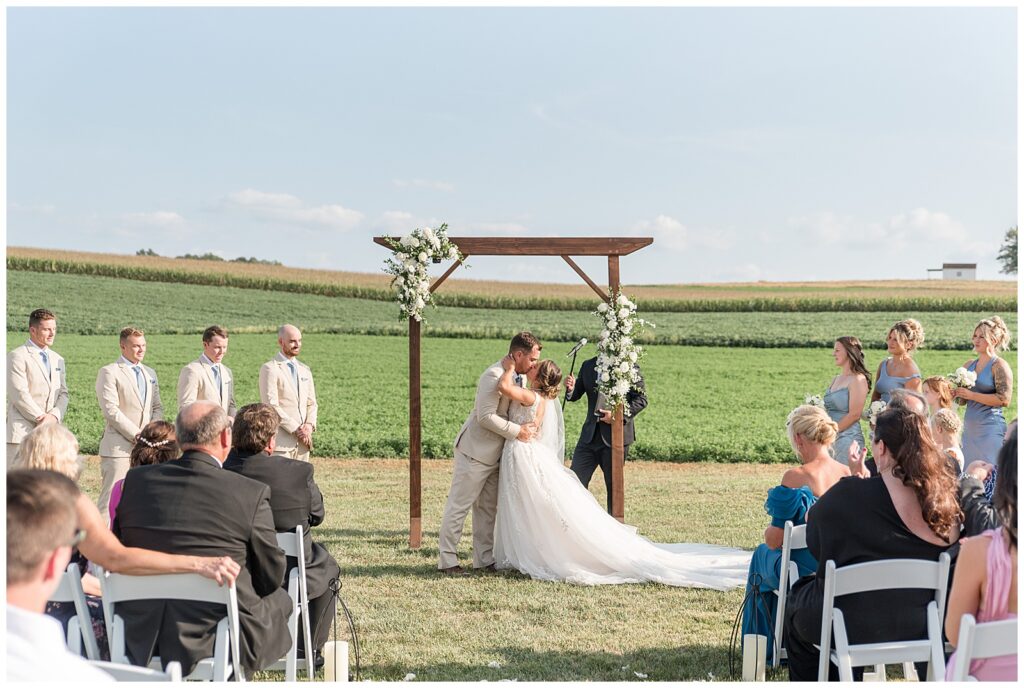 couple sharing their first kiss at outdoor wedding overlooking field at family farm in pennsylvania