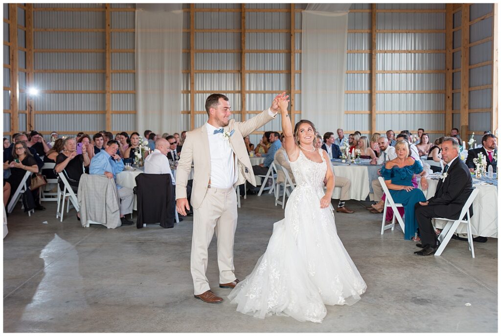 groom twirling his bride under his left hand at indoor barn reception at family farm in pennsylvania