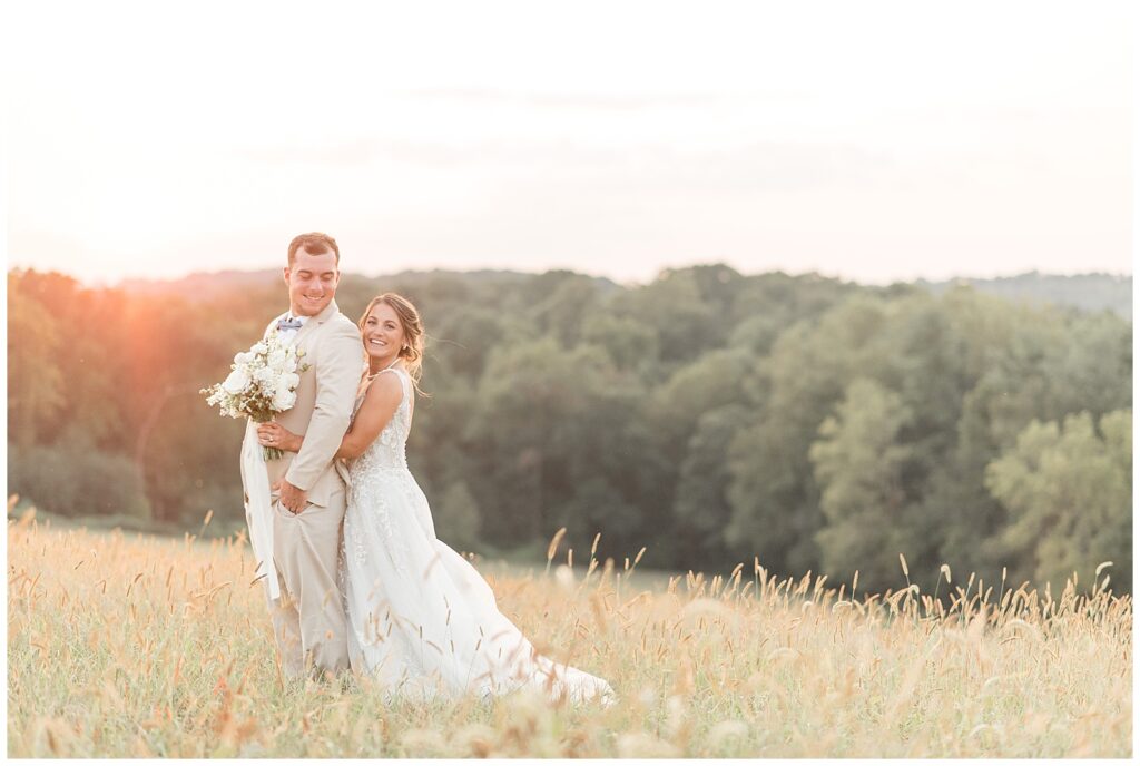 bride standing behind her groom and hugging him in field at sunset at farm in pennsylvania