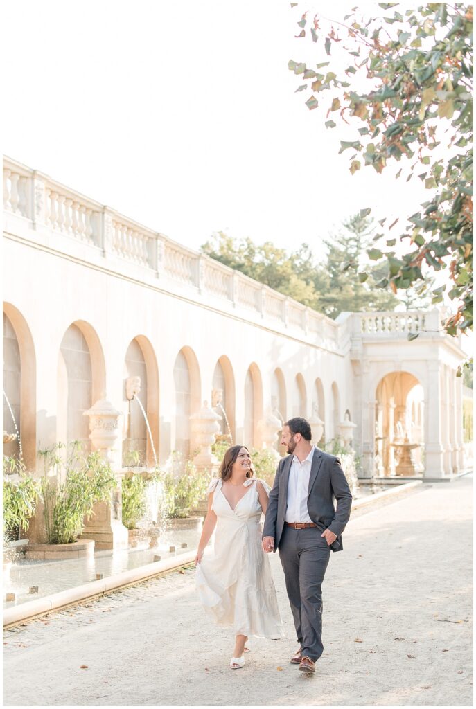 engaged couple holding hands and walking along path by fountains at longwood gardens