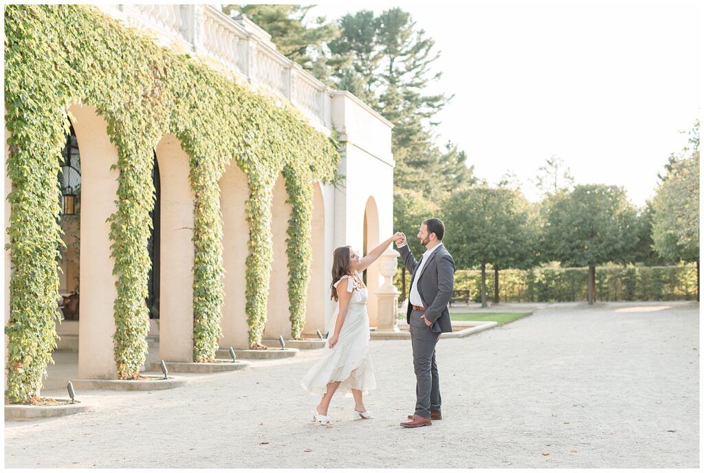 man twirling woman under his left hand by ivy-covered wall at longwood gardens in kennett square pennsylvania