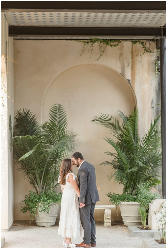 couple kissing with their backs slightly toward camera by arched wall and palm trees in chester county pennsylvania