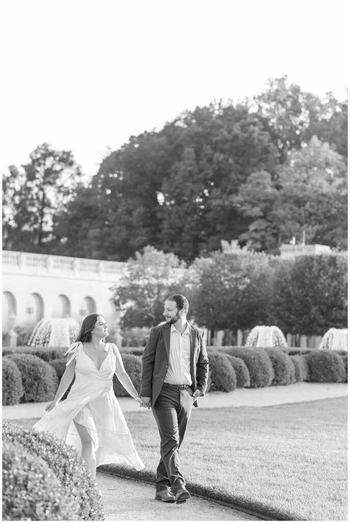 black and white photo of couple holding hands with landscaped yard behind them at longwood gardens