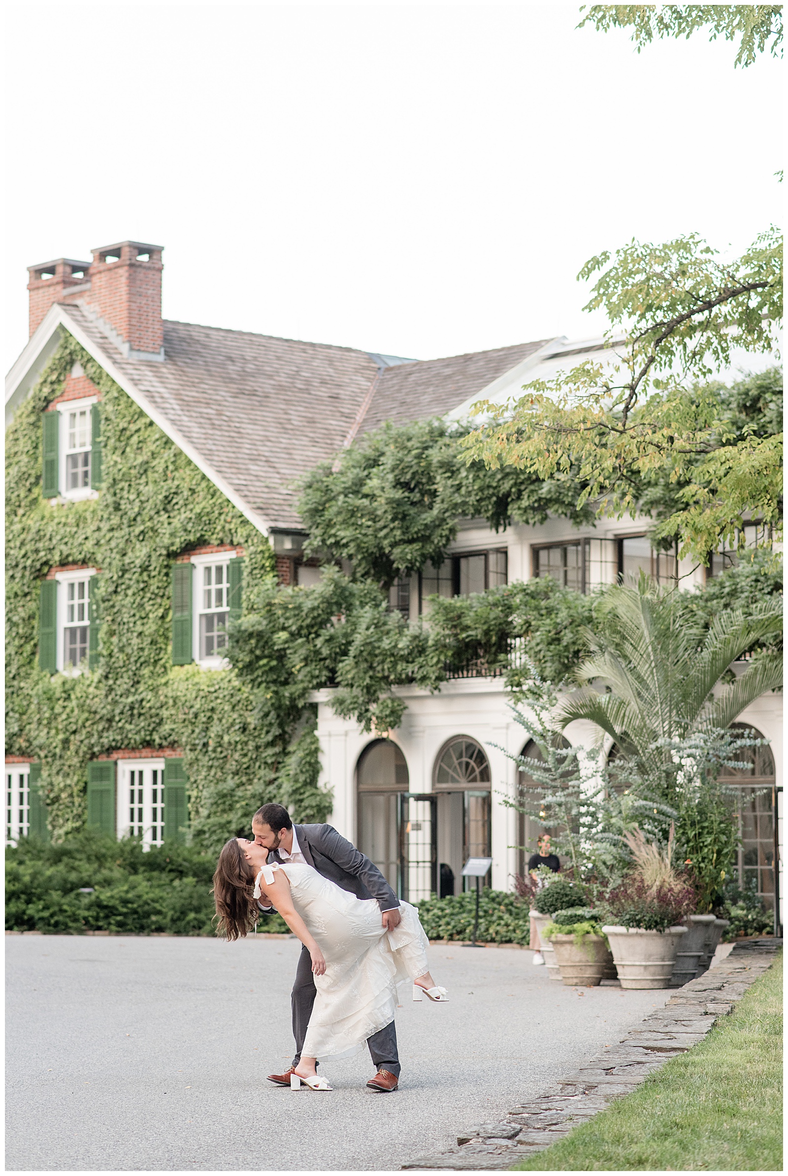 man dipping back woman and kissing her with beautiful ivy-covered house behind them at longwood gardens