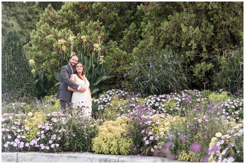 man standing behind woman as he hugs her in flower garden at longwood gardens