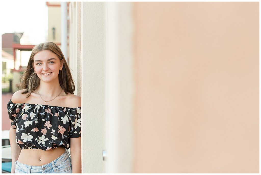 senior girl in black floral tube top and jeans leaning against colorful wall at stoudtburg village