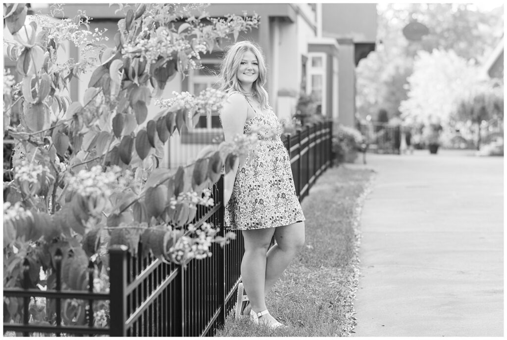 black and white photo of girl leaning against black fence and wearing dress at stoudtburg village