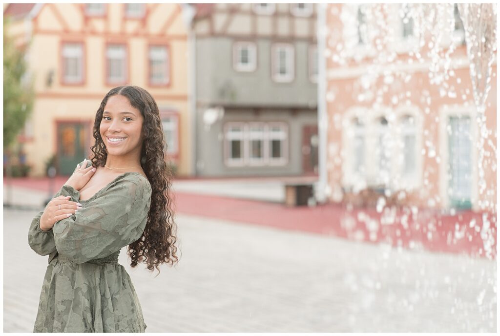 senior girl wearing sage green dress with left shoulder toward camera and german-style buildings behind her in berks county pennsylvania