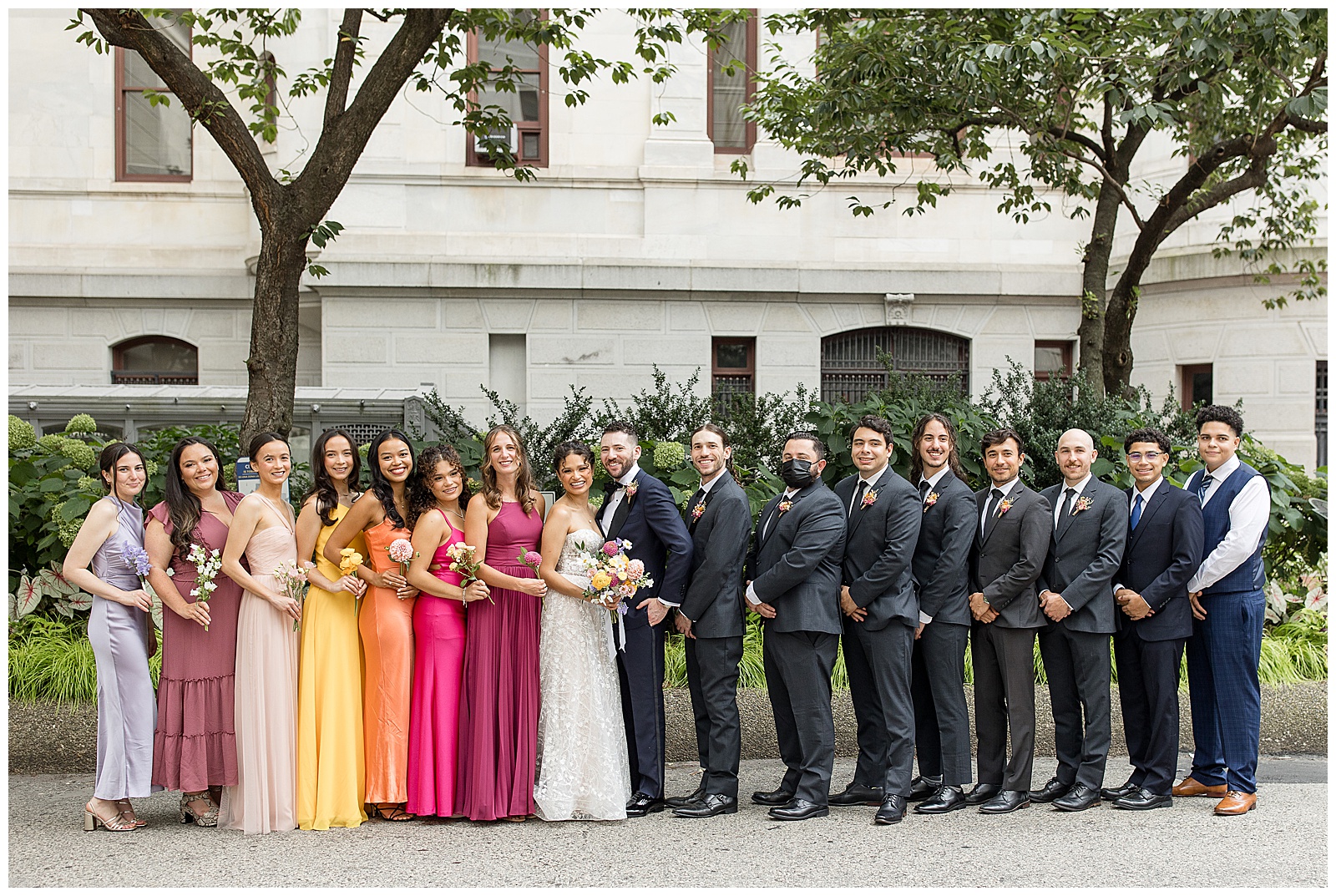 colorful bridal party with bride and groom by white building in downtown philly