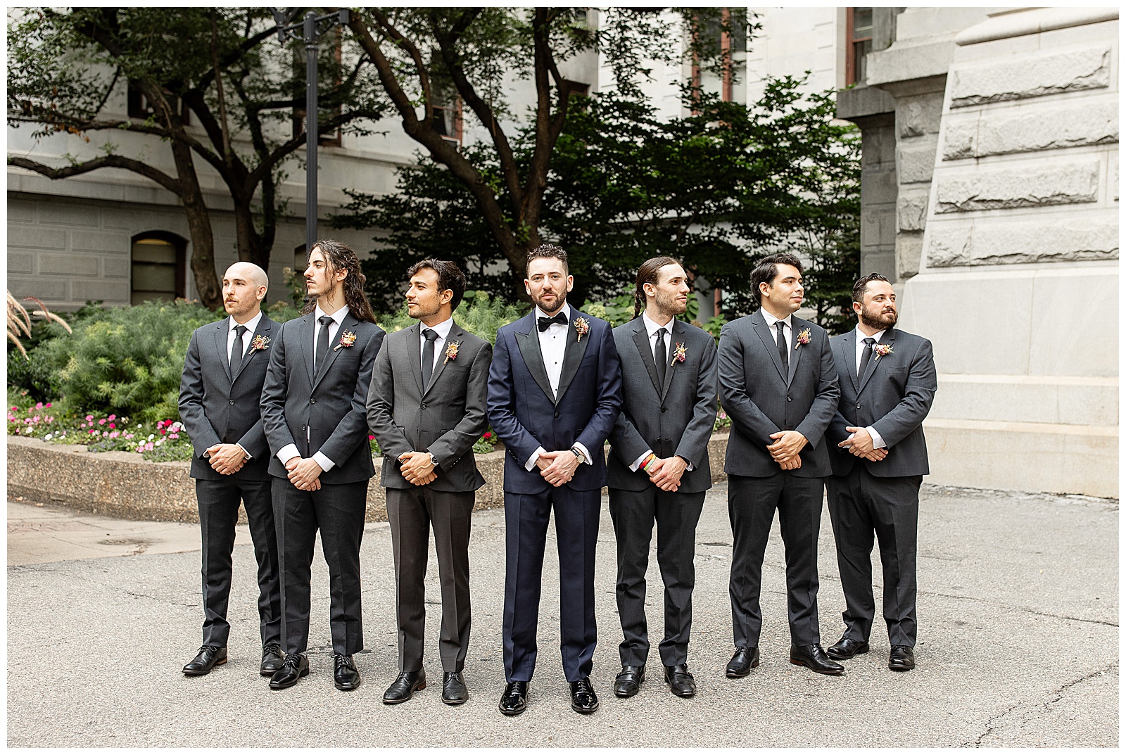 groom with his six groomsmen all wearing dark gray suits with hands folded in front of them as they stand in a v-formation in philly