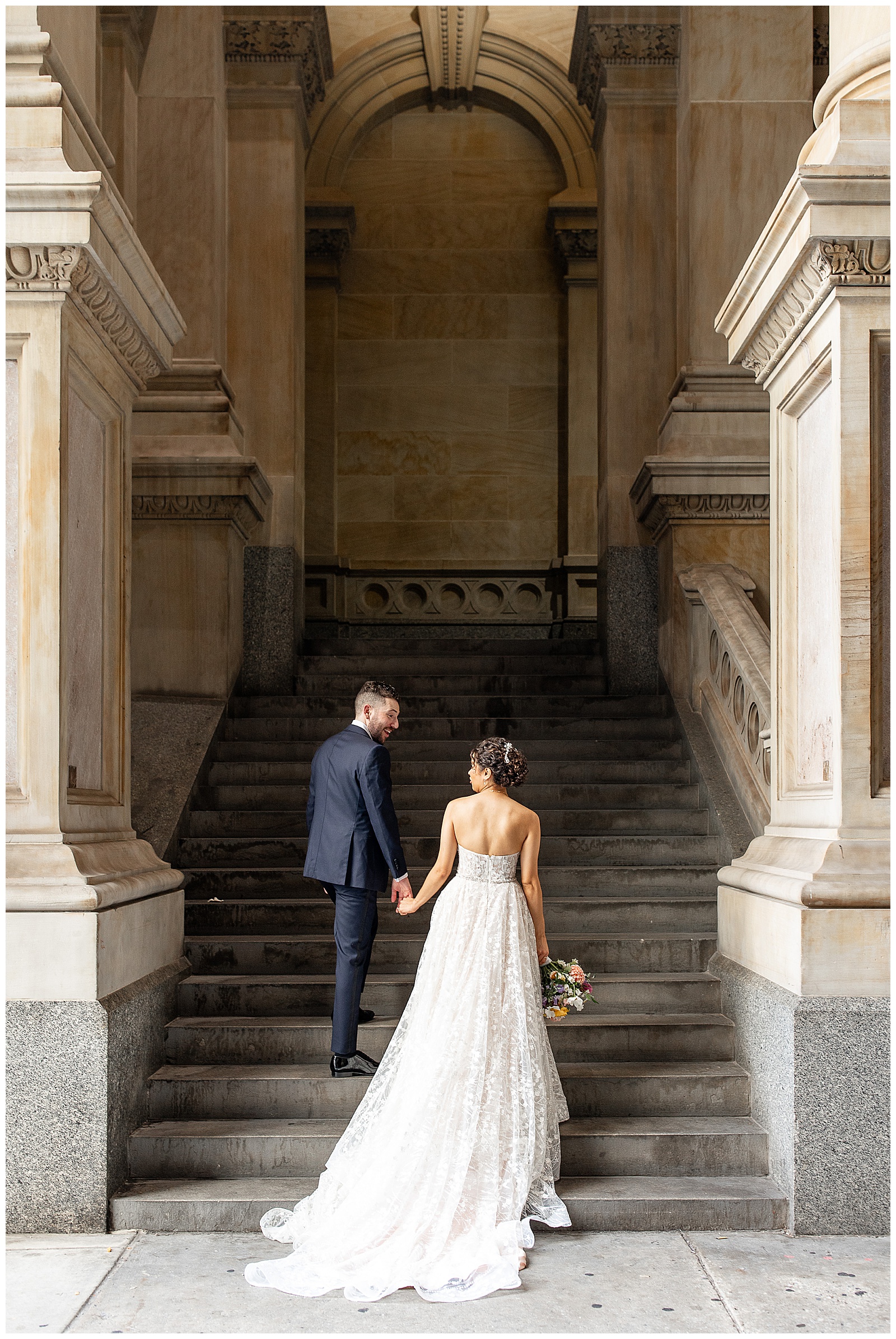 groom holding his bride's left hand as he leads her up large concrete staircase in philadelphia