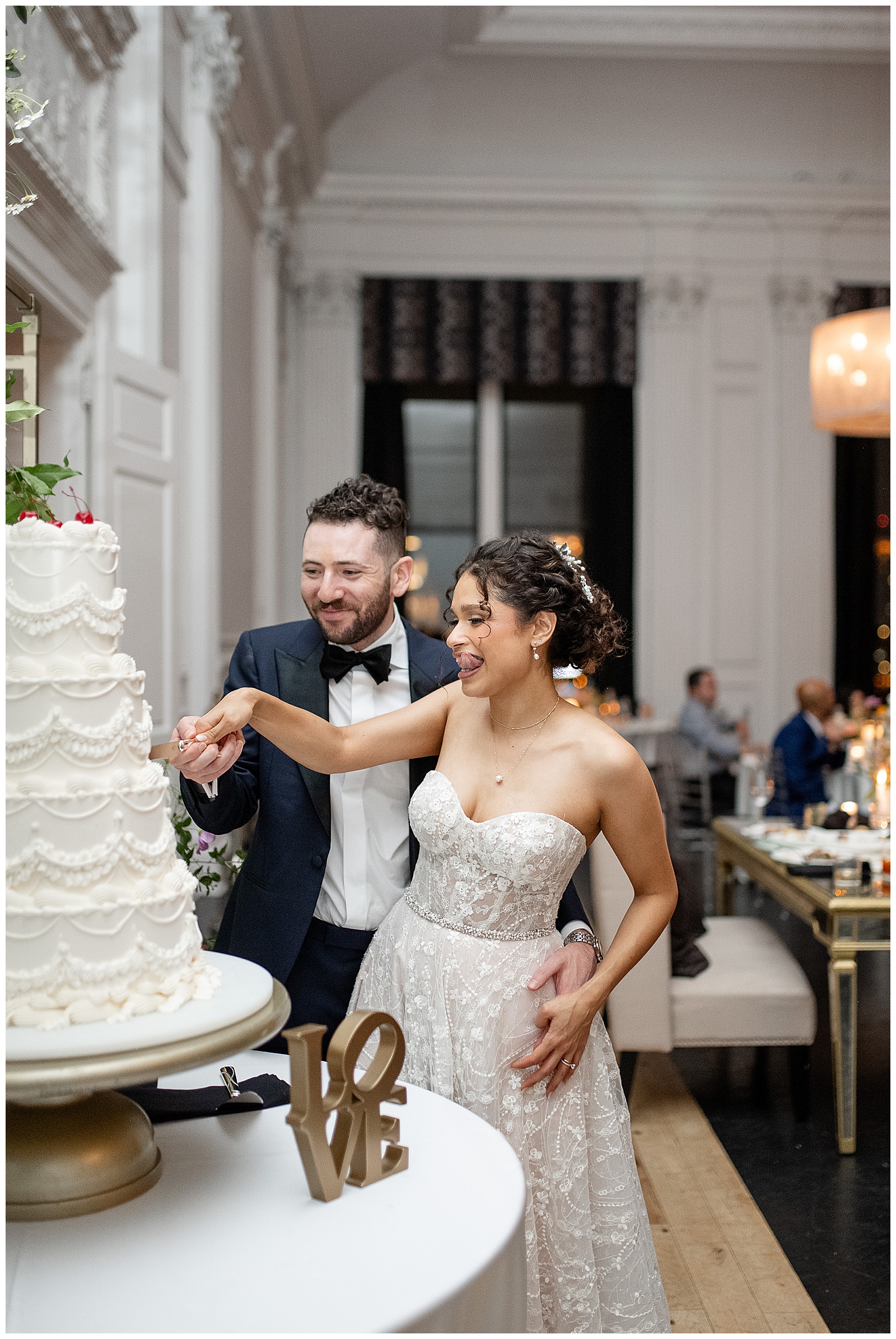 couple working together to cut their tall white wedding cake during reception at cescaphe