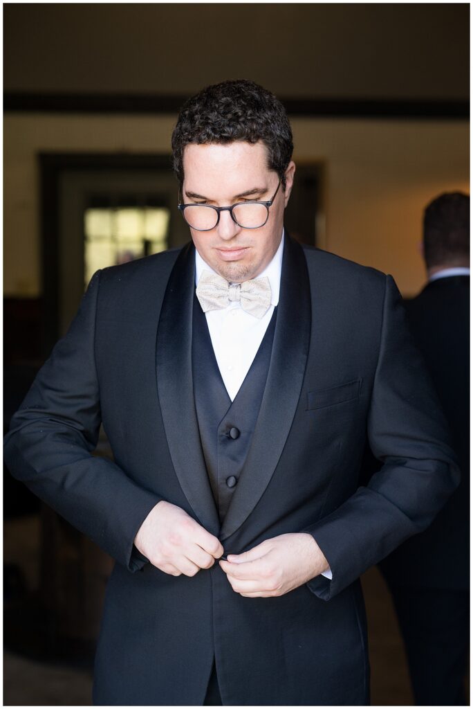 groom looking down as he buttons his black tux coat before wedding at the barn at silverstone