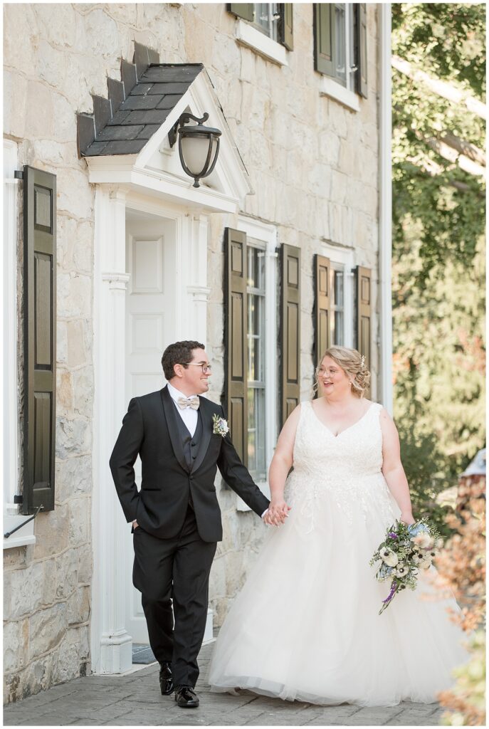 couple holding hands and walking towards camera by stone house at the barn at silverstone