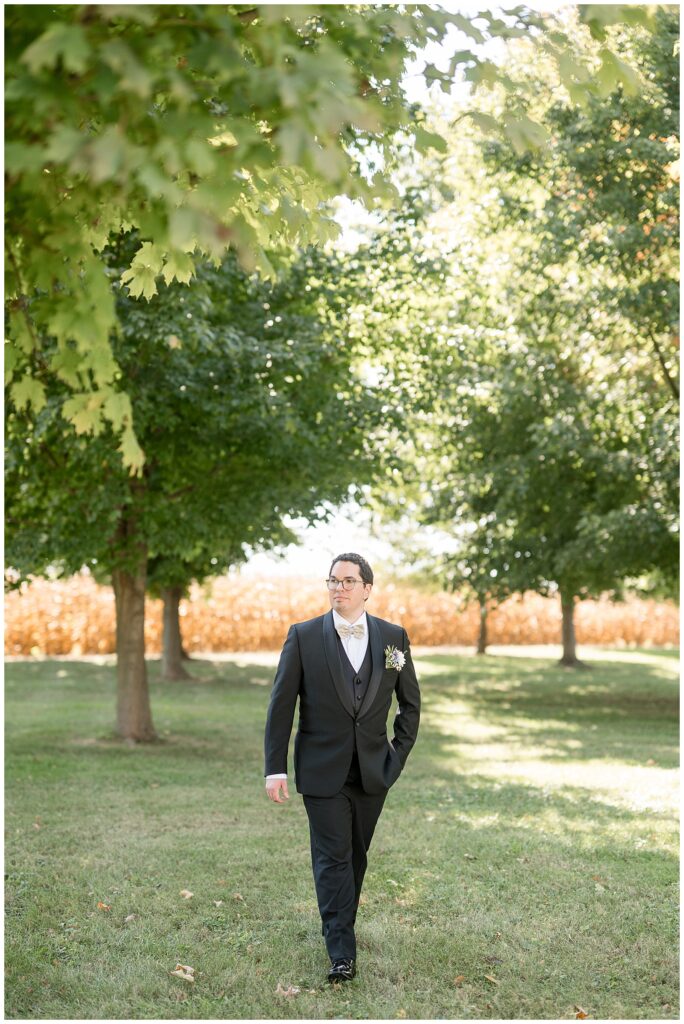 groom walking towards camera with left hand in pocket on sunny fall day in lancaster pennsylvania