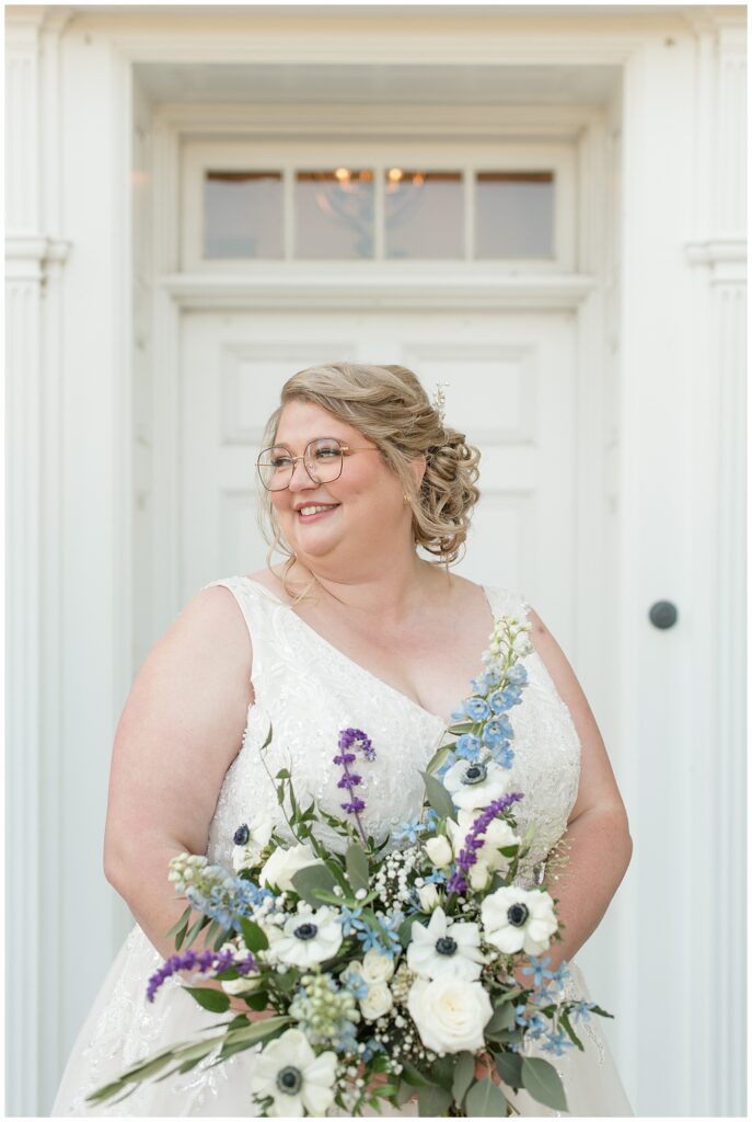 bride holding beautiful bouquet and looking to her right by white door at the barn at silverstone