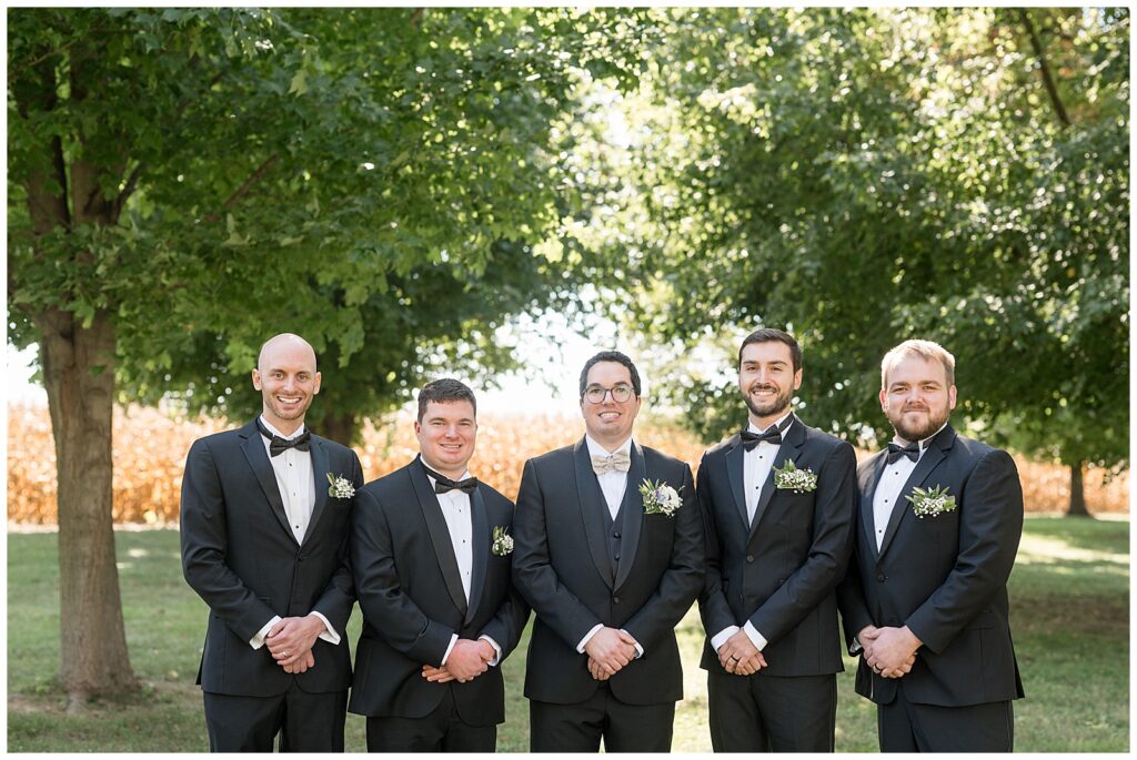 groom with his four groomsmen standing in a row with sunshine peeking through trees behind them in lancaster county