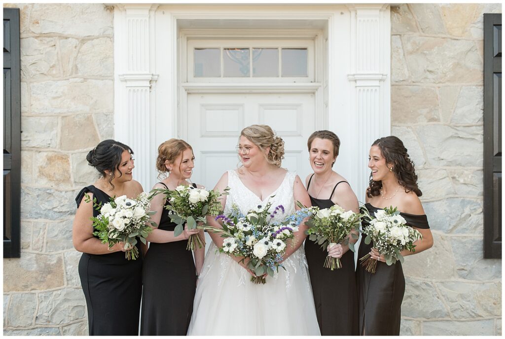 bride with her four bridesmaids wearing black gowns and looking at each other smiling by front door at the barn at silverstone