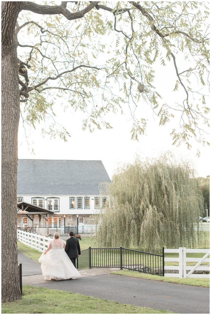 couple walking away from camera on paved pathway heading towards barn reception in lancaster pa