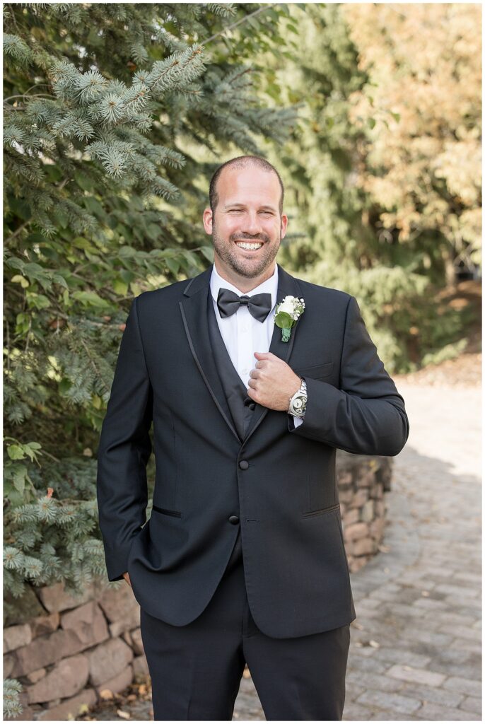 groom in his black tux holding the edge of his suit coat with his left hand and smiling at the camera in gettysburg pennsylvania