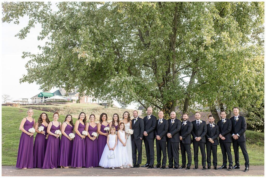 couple with their eight bridesmaids in purple dress, their eight groomsmen in black suits, and two flower girls in white dresses at the links at gettysburg