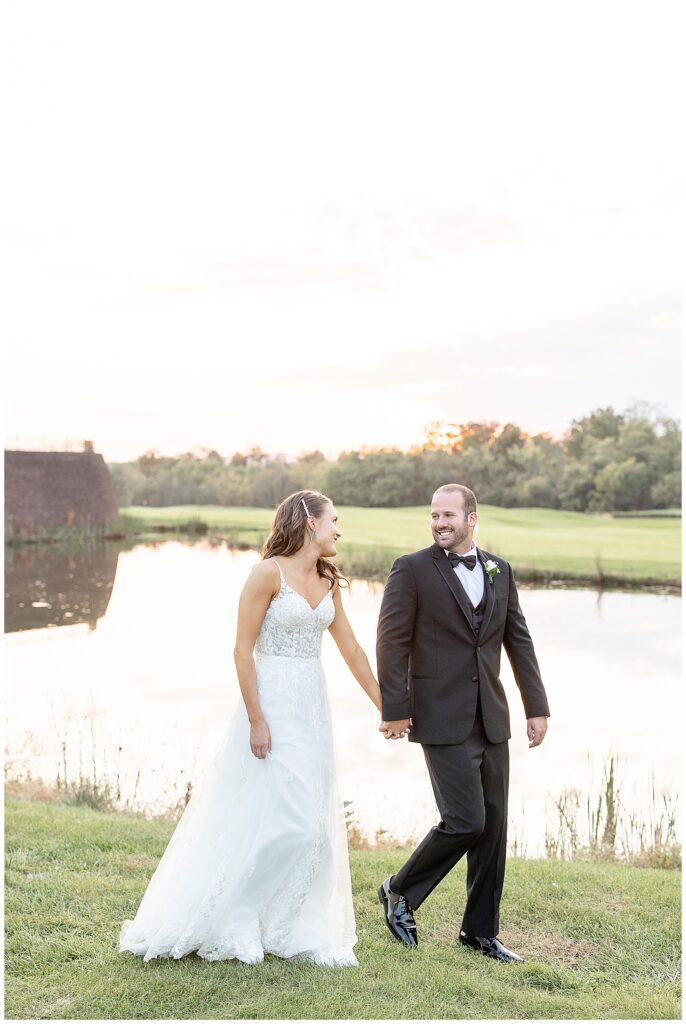 couple holding hands and smiling at each other as they walk along edge of pond at sunset at the links at gettysburg