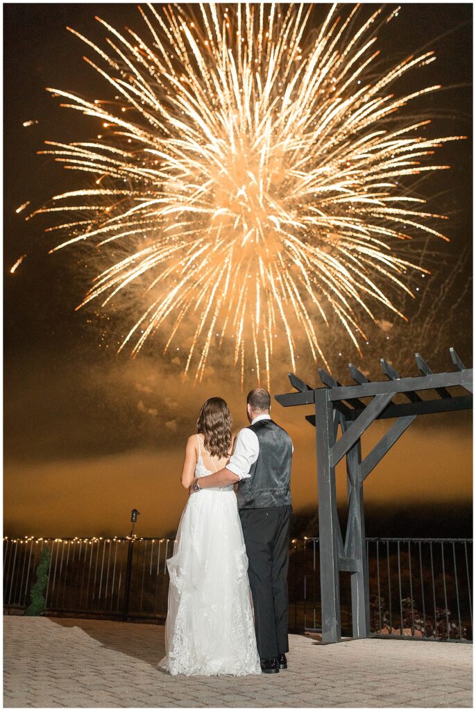 couple with their backs towards the camera as they gaze up at amazing fireworks display at the end of their wedding reception at the links at gettysburg