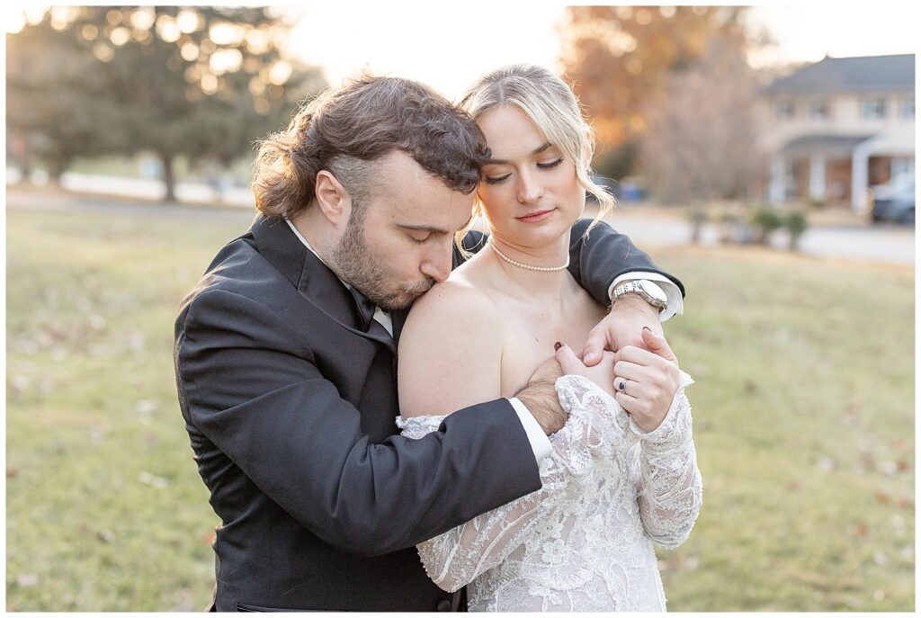 groom hugging his bride from behind and kissing her right shoulder at sunset in york pennsylvania