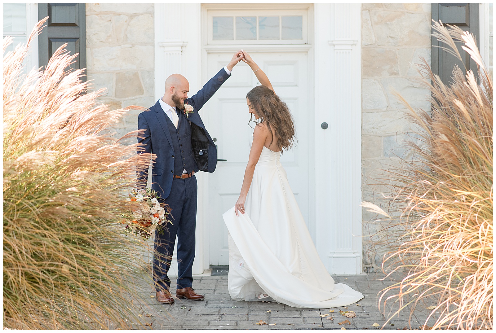 groom twirling his bride under his left hand by white front door at the barn at silverstone