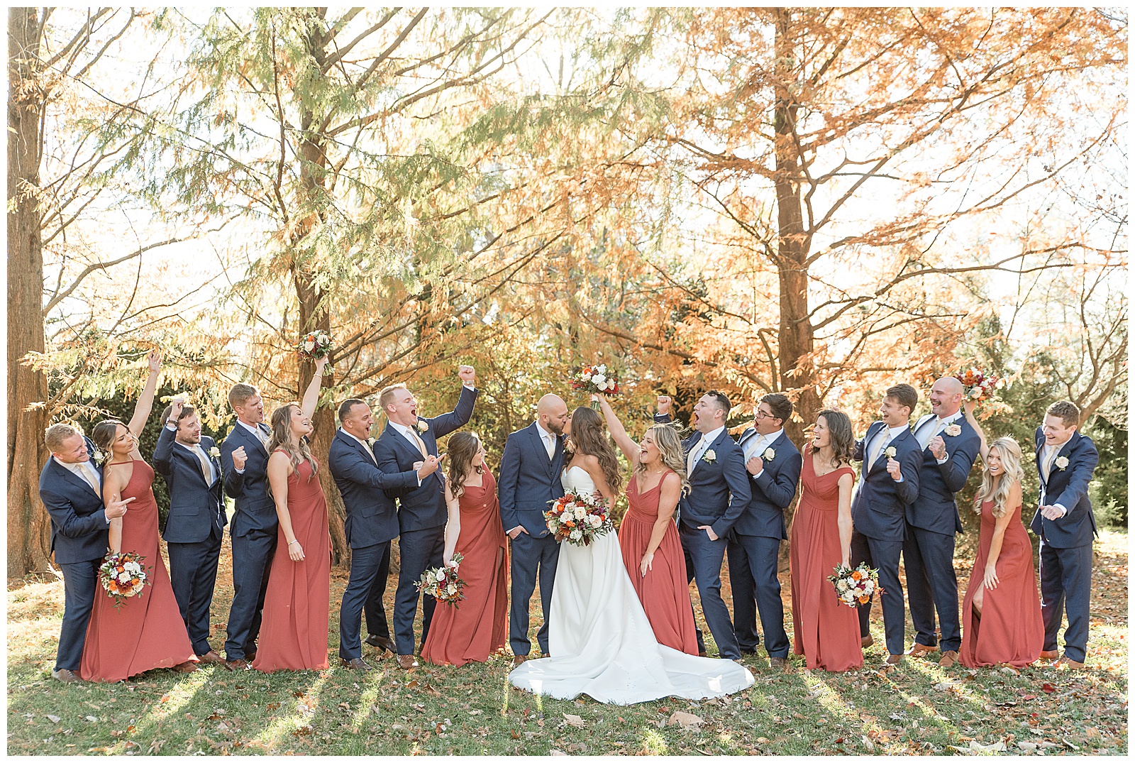 couple kissing as their bridal party surrounds them by colorful trees at the barn at silverstone