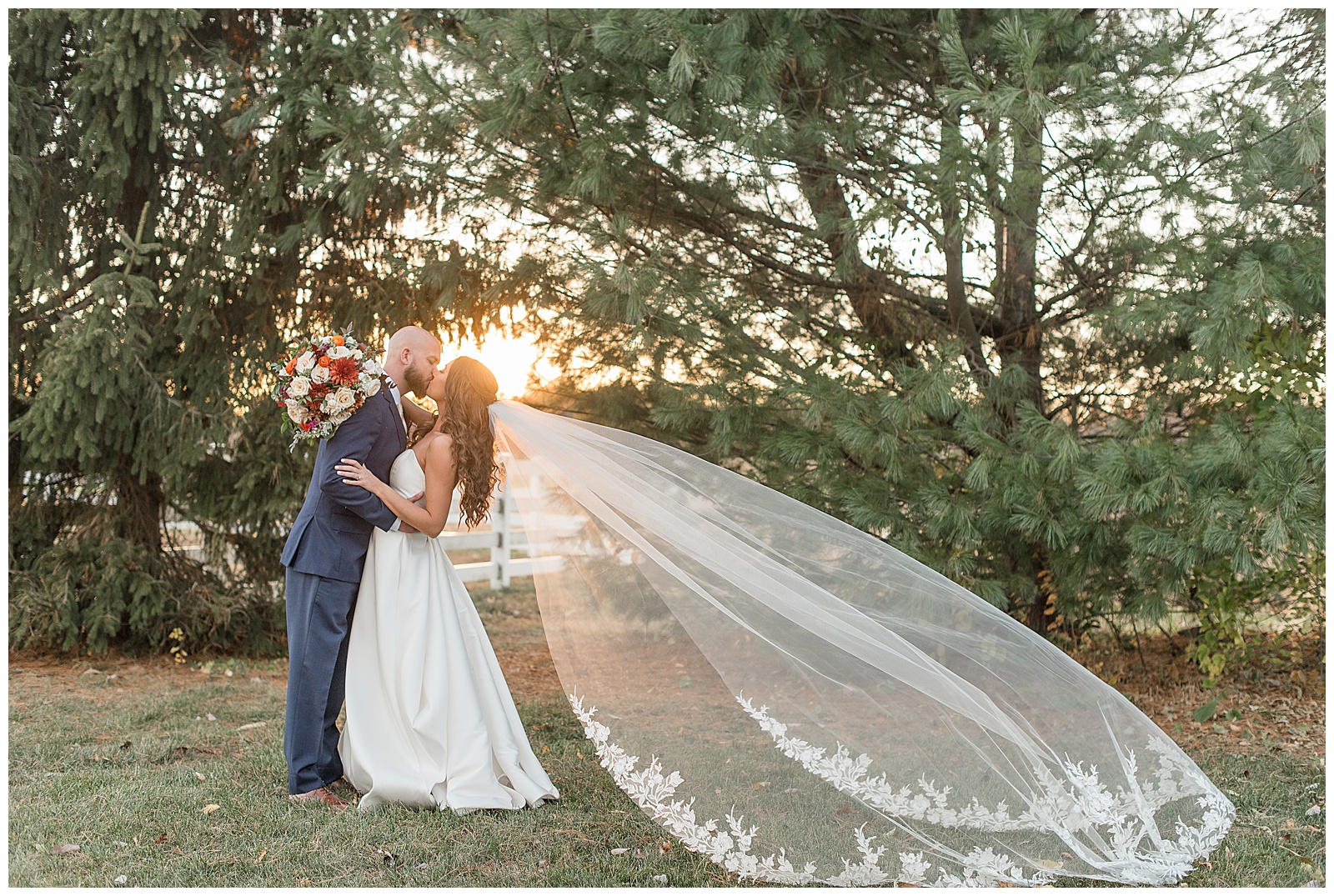 couple kissing with sunset peeking through the trees and bride's long veil extended behind her in lancaster pa