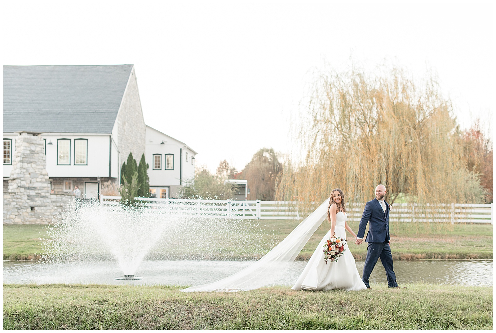 couple holding hands and walking along edge of pond at the barn at silverstone