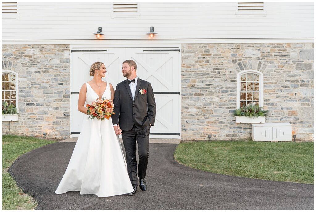 couple looking at each other and walking towards camera with white barn behind them in lancaster county