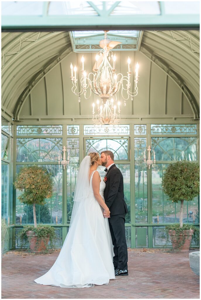 couple kissing inside glass building at the star barn at stone gables estate