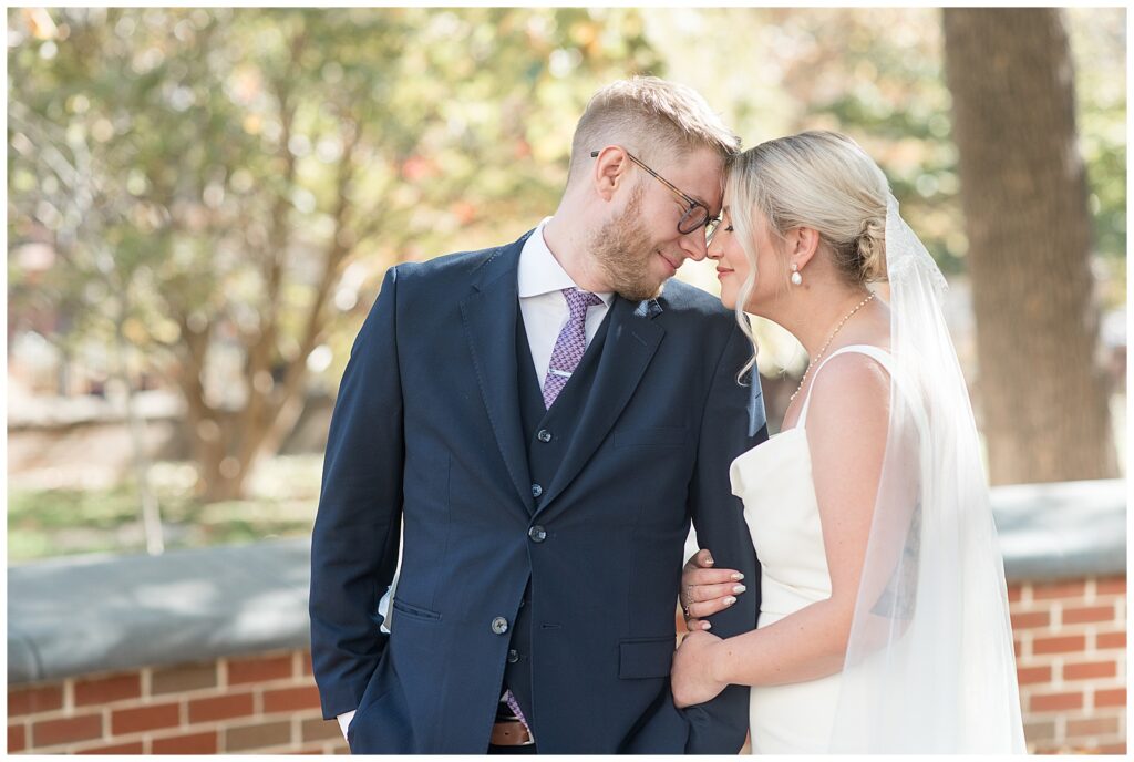 bride holding onto groom's left arm as their foreheads rest together on sunny fall day in philadelphia pennsylvania